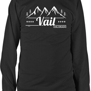 May include: Black long-sleeve shirt with a white graphic design. The design features mountain peaks, pine trees, and the word "Vail" in a stylized font, with "Colorado" below. The shirt has a crew neck and long sleeves.