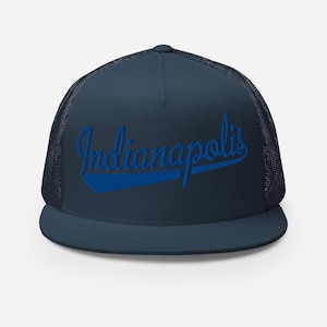 Könnte beinhalten: Eine marineblaue Trucker-Cap mit flachem Schirm und Netzrückseite. Auf der Vorderseite ist das Wort Indianapolis in einer leuchtend blauen Schreibschrift eingestickt, unterstrichen von einer dicken, schrägen blauen Linie ab dem I.