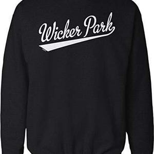 May include: A black long-sleeve crewneck sweatshirt featuring the white text Wicker Park written in a cursive script font with a white underline swoosh extending from the letter k across the chest area of the garment.