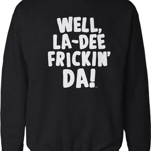 May include: A black long-sleeve crewneck sweatshirt featuring the white text "WELL, LA-DEE FRICKIN' DA!" printed in a bold, rounded sans-serif font across the chest. The garment has a ribbed collar, cuffs, and hem, with a solid black fabric finish.