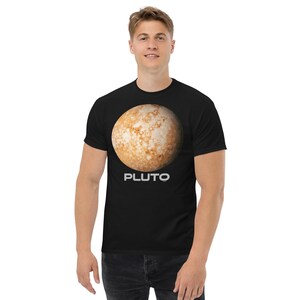 Może przedstawiać: Czarny t-shirt z krótkim rękawem z dużą, szczegółową grafiką planety Pluton w odcieniach brązu, beżu i bieli. Słowo PLUTO jest nadrukowane wyraźną, białą czcionką bezszeryfową bezpośrednio pod ilustracją przedstawiającą planetę.