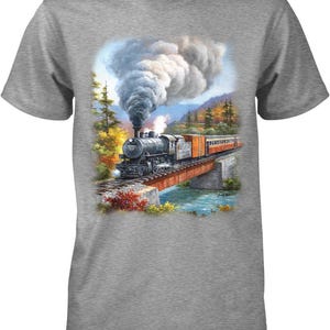 May include: A heather gray short-sleeve t-shirt featuring a graphic print of a black steam locomotive crossing a bridge over a river. The train emits a large plume of gray smoke, set against a backdrop of autumn trees and mountains.