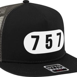 May include: Black trucker hat with a white oval patch that says "757" on it. The hat has a mesh back and a black snap closure.
