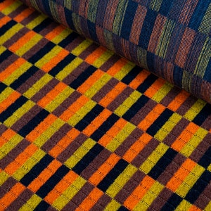 May include: Close-up of two fabric swatches with checkered patterns. The top swatch is a dark blue with thin orange and green stripes. The bottom swatch is a brown, orange, yellow, and black checkered pattern.