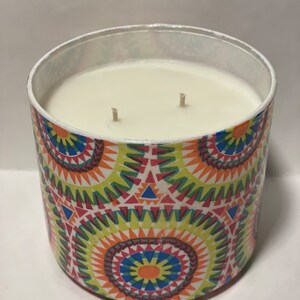 May include: A white candle with two wicks in a colorful, geometric patterned jar. The jar has a white top and a colorful, geometric pattern on the bottom. The pattern is made up of circles, triangles, and squares in shades of red, orange, yellow, green, blue, and purple.