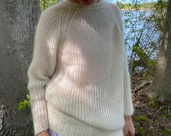 May include: A white, lightweight knit sweater with a round neckline and long sleeves. The sweater is made of a delicate, airy yarn and has a slightly loose fit.