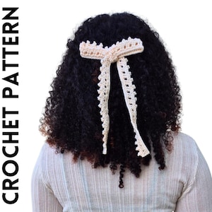 May include: A crocheted hair bow in a cream colour with a simple design. The bow is tied in a knot and has two long tails.