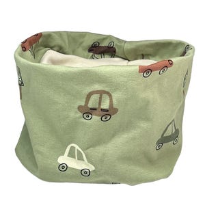 May include: A sage green fabric neck warmer featuring a repeating pattern of hand-drawn style cars in shades of brown, cream, and dark green. The interior lining is a solid cream colour. The text kinnerleev is printed in black in the bottom right corner.