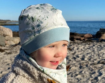 Puede incluir: Un niño lleva una boina de color blanco y verde con estampado floral, con un borde azul claro y un cuello de lana a juego con estampado floral blanco y verde. El niño lleva una chaqueta de forro polar marrón claro.