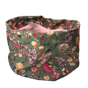 Könnte beinhalten: Ein Nackenwärmer mit floralem Muster mit grünem Hintergrund und rosa Innenfutter. Der Stoff ist mit einer Vielzahl farbenfroher Blumen bedeckt, darunter rosa, gelbe und lila Blüten. Der Nackenwärmer ist zum Tragen um den Hals konzipiert.