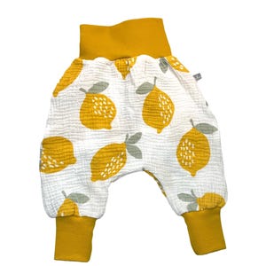 May include: Baby trousers featuring a white fabric patterned with yellow lemons and grey leaves. The cuffs and waistband are mustard yellow. The cursive text "kinnerleev" is at the bottom.