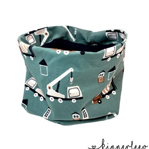 Könnte beinhalten: Ein türkisfarbener Stoff-Halswärmer mit einem sich wiederholenden Muster aus Baufahrzeugen und Gebäuden. Das Muster umfasst Kräne, LKWs und Häuser.