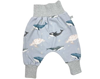 Puede incluir: Pantalones de bebé azul claro con estampado de ballena y tortuga. Los pantalones tienen una cintura y puños elásticos grises.