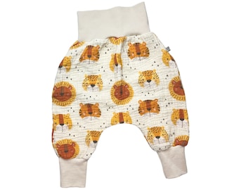 Könnte beinhalten: Weiße Babyhose mit einem Löwen- und Tigerdruck. Die Hose hat einen breiten elastischen Bund und gekrempelte Beine.