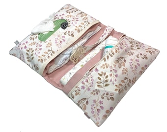 Könnte beinhalten: Eine Wickeltasche mit floralem Muster in Rosa und Weiß mit mehreren Taschen und einem Reißverschluss. Die Tasche ist geöffnet und enthält eine Windel, Feuchttücher und eine kleine Flasche Lotion.