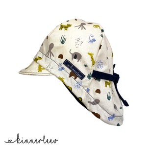 Op de afbeelding: Een witte zonnehoed met een blauwe rand en een donkerblauwe stropdas. De hoed heeft een patroon van dieren, waaronder olifanten, giraffen en tijgers, in tinten geel, bruin en blauw. De tekst "Adventure" is op de hoed gedrukt.