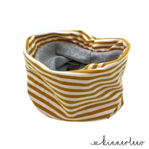 Könnte beinhalten: Ein gelber und weiß gestreifter Stoff-Halswärmer mit grauem Futter. Der Halswärmer ist in der Mitte gefaltet und liegt auf einem weißen Hintergrund.