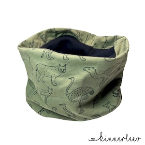Könnte beinhalten: Ein grüner Stoff-Halswärmer mit schwarzem Futter. Der Stoff hat ein Muster aus verschiedenen Tieren, darunter ein Strauß, ein Luchs und ein Kamel.