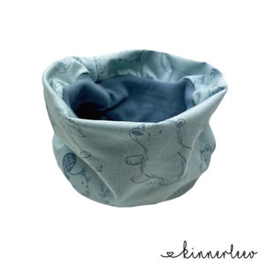 Könnte beinhalten: Ein hellblauer Halsschmeichler mit einem blau-weißen Muster aus Bären, Eichhörnchen und anderen Waldtieren. Der Halsschmeichler ist aus weichem, dehnbarem Stoff gefertigt und perfekt, um sich im Winter warm zu halten.