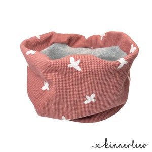 Könnte beinhalten: Ein rosa Waffelstrick-Halswärmer mit einem weißen Vogelmuster. Der Halswärmer ist reversibel und hat ein graues Fleecefutter.