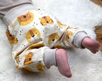 Könnte beinhalten: Weiße Babyhose mit einem Muster aus orangefarbenen und braunen Tiergesichtern. Die Hose hat einen beigefarbenen Bund am unteren Ende.