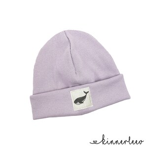 Può includere: Un berretto di lana color lavanda con una toppa grafica a forma di balena. Il berretto è realizzato in un tessuto morbido e a coste.