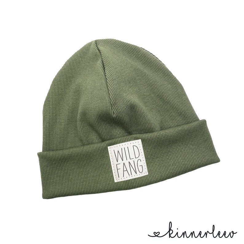 Puede incluir: Un gorro de punto verde con un parche blanco que dice "WILD FANG" en letras negras.