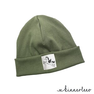 Puede incluir: Un gorro de punto verde con un parche blanco que muestra una ilustraci&oacute;n en blanco y negro de un caballo alado.