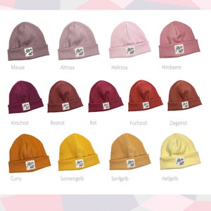 Op de afbeelding: Een set van 12 mutsen in verschillende kleuren, waaronder mauve, roze, rood, oranje en geel. Elke muts heeft een klein wit label met de tekst "Ahm no" erop.