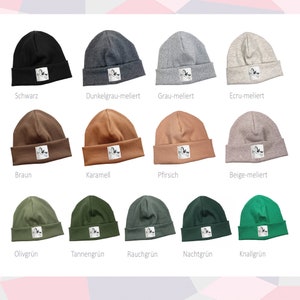 Può includere: Dieci berretti di lana di diversi colori con una piccola toppa bianca sul davanti. I berretti sono di colore nero, grigio scuro, grigio chiaro, beige, marrone, caramello, pesca, verde oliva, verde scuro e verde brillante.