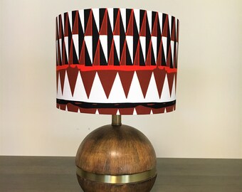May include: A wooden table lamp with a round base and a red, white, and black geometric patterned lampshade.