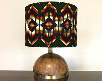 May include: A table lamp with a wooden base and a green lampshade with a geometric pattern in red, yellow, and white.