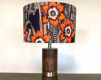 May include: A table lamp with a brown wooden base and a floral lampshade. The lampshade features a pattern of orange and white flowers on a beige background.
