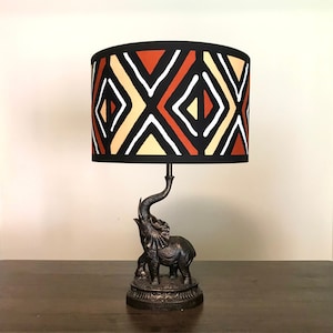 May include: A table lamp with a black and white geometric patterned lampshade and a bronze elephant base.
