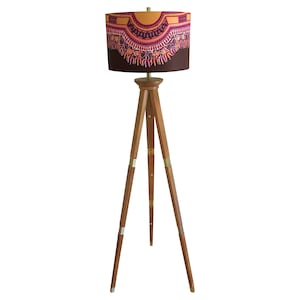 May include: A tripod floor lamp with a brown lampshade featuring a colourful geometric pattern. The lampshade has a gold trim and the tripod base is made of wood.