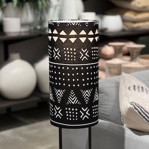 May include: A black and white patterned lamp with a cylindrical shade and a concrete base. The lamp has a black metal stand.