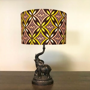 May include: A table lamp with a brown, pink and yellow patterned lampshade. The lamp base is an elephant sculpture with an upturned trunk.
