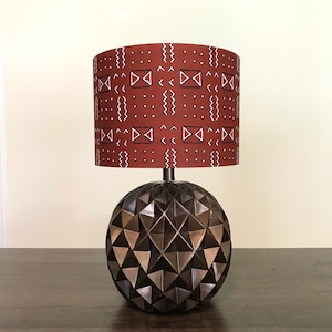 May include: A table lamp with a geometric base and a rust-colored lampshade with a white geometric pattern.