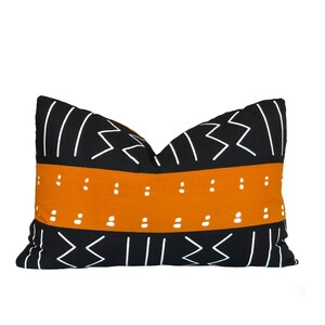 Könnte beinhalten: Schwarzes und orangefarbenes Kissen mit geometrischem Muster. Das Kissen hat einen weißen Streifen mit einem sich wiederholenden Punktmuster.
