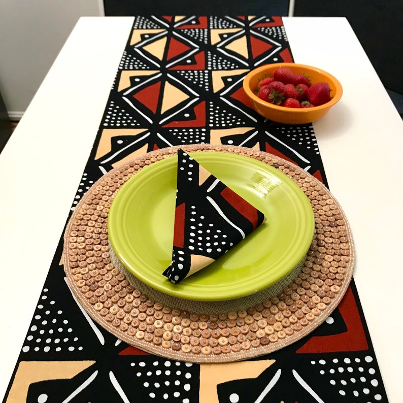 Peut inclure: Un chemin de table noir, blanc, rouge et beige avec un motif g&eacute;om&eacute;trique. Une assiette verte avec une serviette noire, blanche et rouge est pos&eacute;e sur un dessous de plat en osier. Un bol de fraises rouges est sur la table.