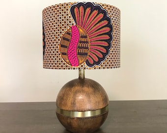 May include: A table lamp with a wooden base and a fabric lampshade. The lampshade has a geometric pattern in shades of orange, pink, black, and white.