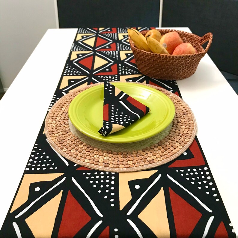 Peut inclure: Un chemin de table noir, rouge et beige avec un motif g&eacute;om&eacute;trique. Une assiette verte avec une serviette &agrave; motif noir et blanc est pos&eacute;e sur un dessous de plat en osier.