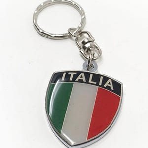 May include: A silver keyring with a shield-shaped charm featuring the Italian flag and the word "ITALIA" in black lettering.
