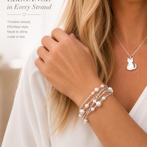 May include: A multi-strand bracelet featuring white pearls and small silver-toned beads, paired with a silver-toned necklace featuring a cat-shaped pendant. The image includes the text: ELEGANCE in Every Strand. Timeless beauty. Effortless style.