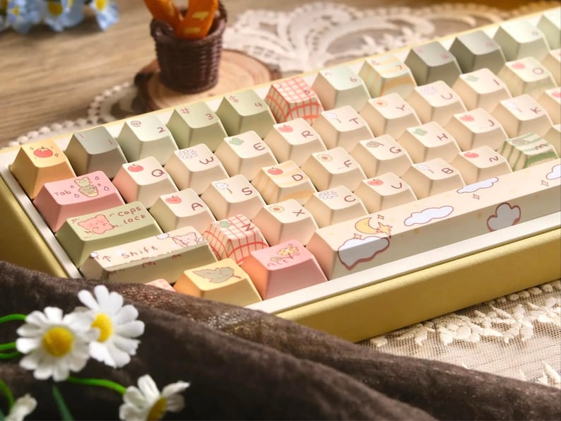 May include: A mechanical keyboard with custom keycaps in pastel shades. The keycaps are decorated with illustrations of fruits, animals, and patterns. The keyboard has a yellow frame and is set against a soft, neutral background.