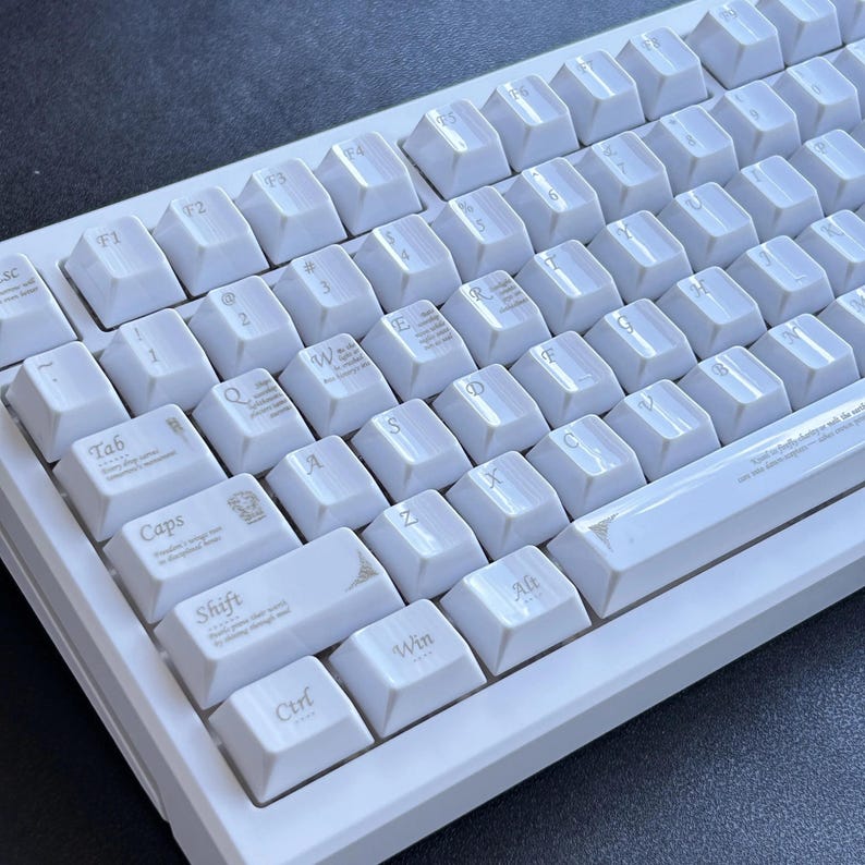 Może przedstawiać: Biała klawiatura mechaniczna z białymi nakładkami na klawisze. Klawiatura ma standardowy układ QWERTY z klawiszami funkcyjnymi i klawiaturą numeryczną. Klawisze są czyste, a klawiatura jest w dobrym stanie.