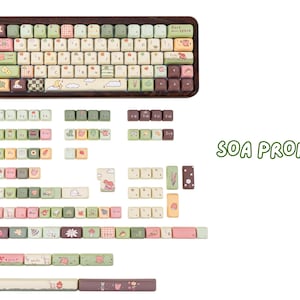 May include: A keyboard with a wooden frame and a variety of colourful keycaps. The keycaps feature pastel colours and cute illustrations of animals, plants, and patterns. Additional keycaps are displayed below the keyboard.