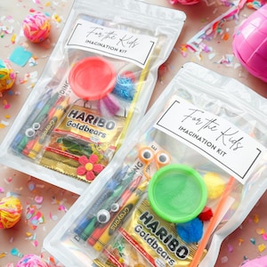 May include: Two clear plastic bags labeled "For the Kids IMAGINATION KIT" filled with crayons, play dough, googly eyes, and Haribo Goldbears candy. The bags are surrounded by colorful confetti and decorative balls.