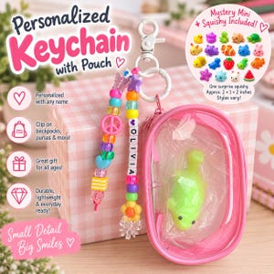 May include: A personalized keychain featuring a white plastic clip, two beaded strands with colorful plastic beads, and a clear pink oval zippered pouch containing a small green squishy toy. The beads include a flower, a peace sign, and letter cubes spelling OLIVIA.