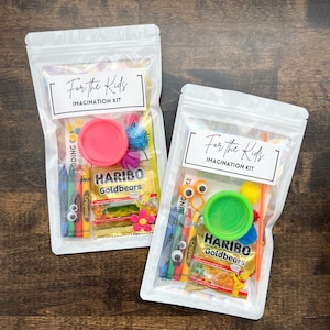 May include: Two clear pouches labeled "For the Kids IMAGINATION KIT" filled with colorful craft supplies. Each kit includes crayons, playdough, googly eyes, pom-poms, and a package of Haribo Goldbears gummy candies.